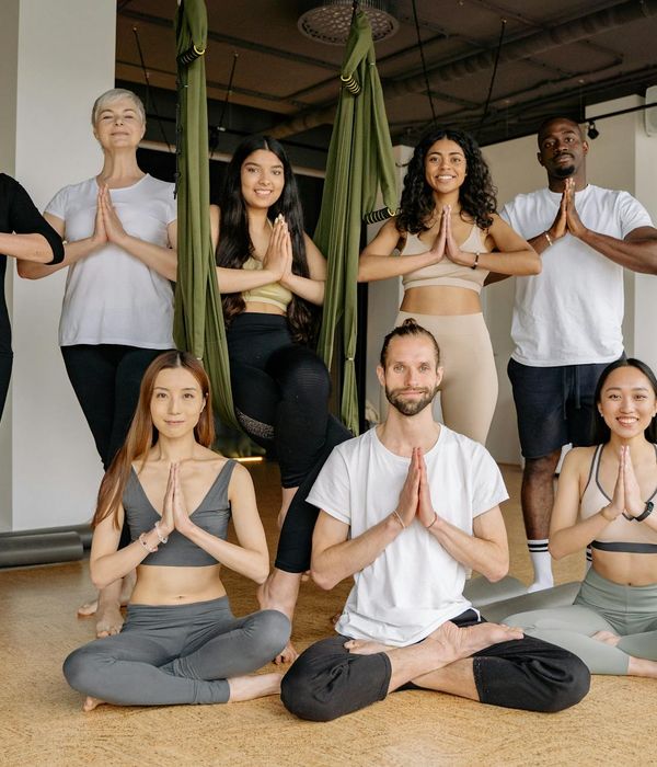 A group of teenagers practicing a balancing yoga pose together in a studio.